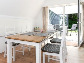 Een eetgedeelte met een houten tafel, witte stoelen en een schuifdeur naar een terras.