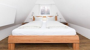 Une chambre à coucher avec un lit en bois, du linge de lit blanc, une fenêtre et une table de chevet.