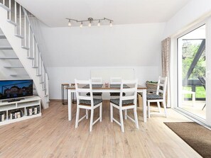 Ruokailutila, jossa on valkoinen pöytä ja tuolit, jalustalla oleva televisio ja portaikko.
