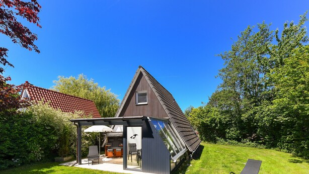Une maison moderne avec un toit en pente, un patio couvert avec des meubles d’extérieur et une pelouse.