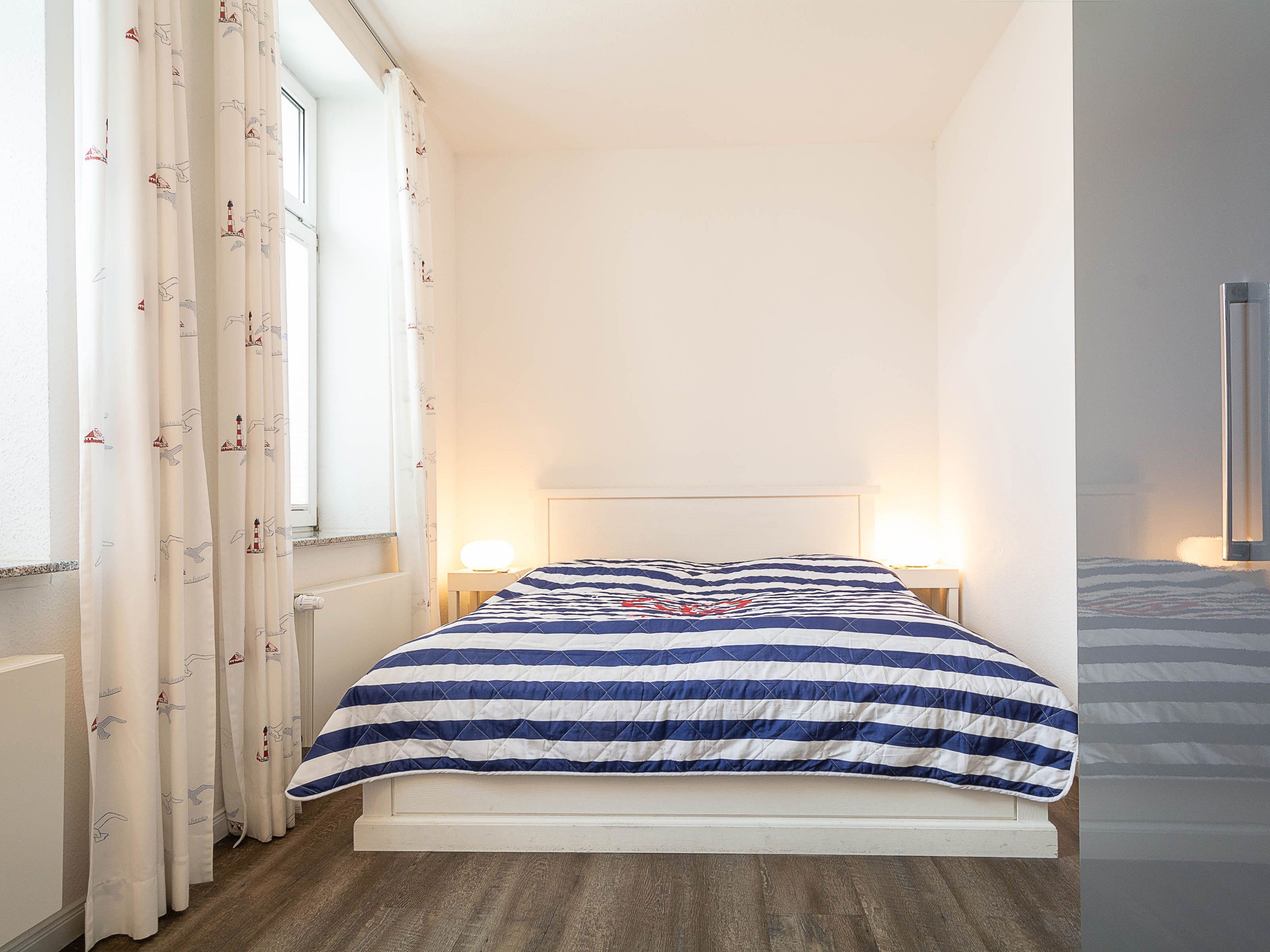 Un dormitorio con cama, cortinas, lámparas de noche y una ventana.