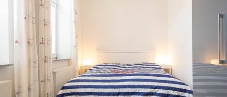 Un dormitorio con cama, cortinas, lámparas de noche y una ventana.