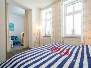A bedroom with a bed, a standing lamp, a window with curtains, a blue chair, and a door leading to another room. - 24-08 - resort Villa Apt 24-08. (Kühlungsborn)