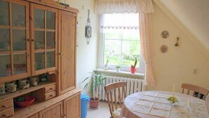A dining area with a round table, wooden cabinets, and a window with curtains. - Apartment 1 - Rügen-Fewo 249 (Sellin)