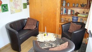 A cozy living room with a brown leather sofa, a round leather chair, and a coffee table with a candle. There is a wooden bookshelf with books and decorative items. - Apartment 1 - Rügen-Fewo 249 (Sellin)