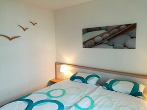A neatly made bed with a patterned bedspread, a bedside lamp, and a wall-mounted picture of stones.