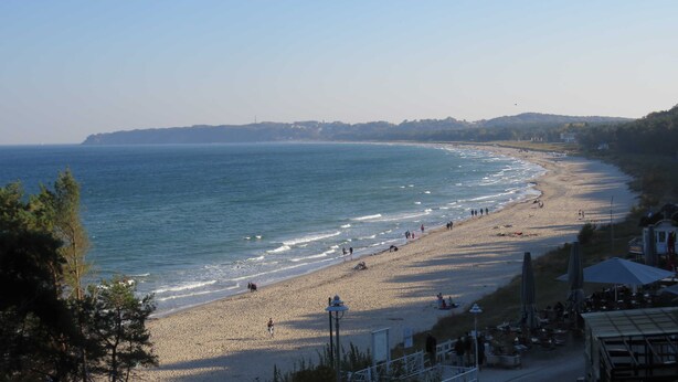 Uma praia com vista clara do oceano, uma faixa de areia e alguns edifícios ao fundo.