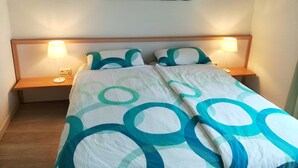 Uma cama bem arrumada com um edredom estampado, duas luminárias de cabeceira e um quadro na parede.