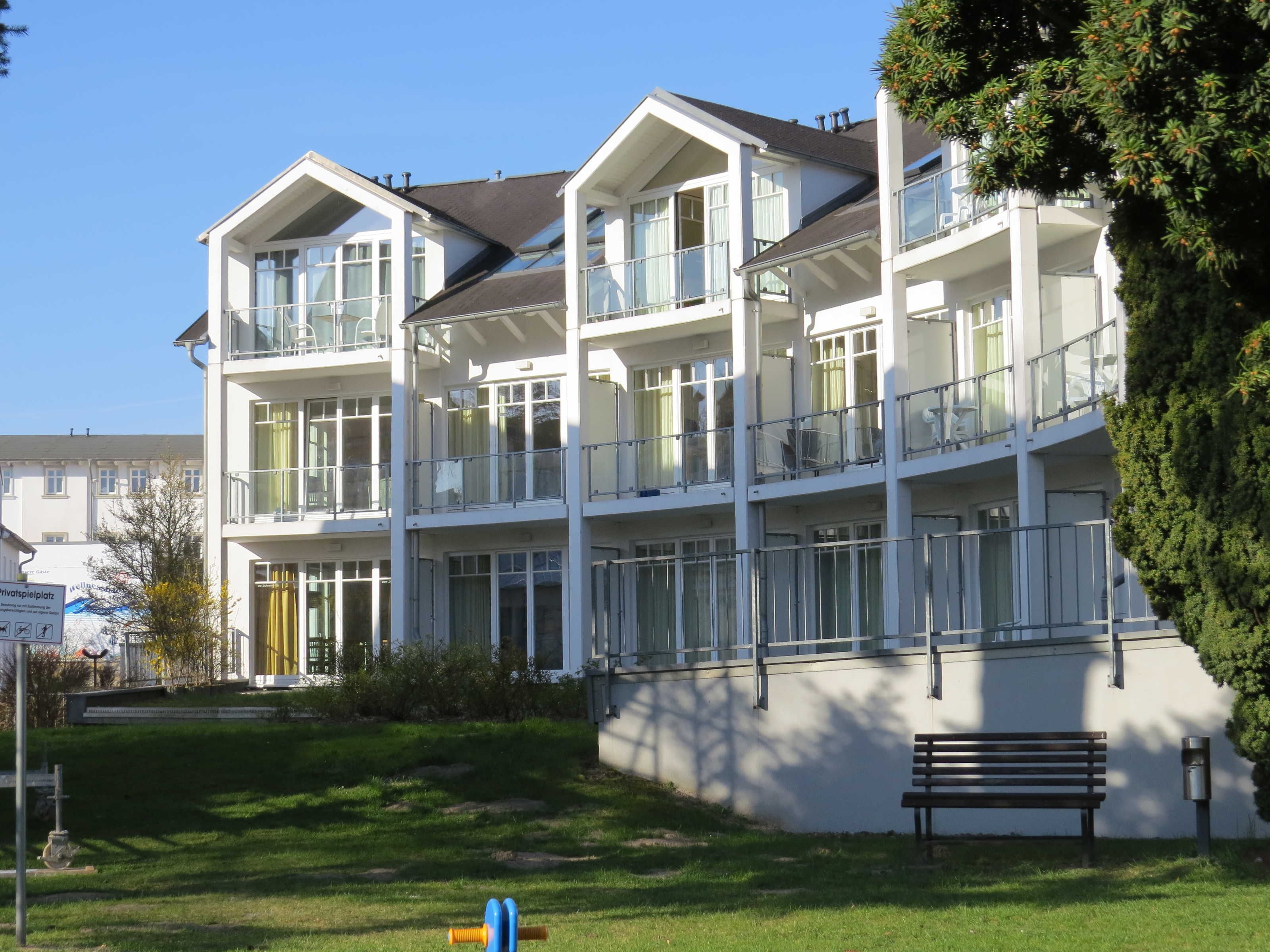 A multi-story residential building with balconies, large windows, and a grassy lawn.