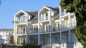 Um edifício residencial com vários andares, varandas, janelas amplas e um gramado.