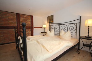 A bed with a headboard, two bedside tables with lamps, a brick wall, and a painting on the wall.