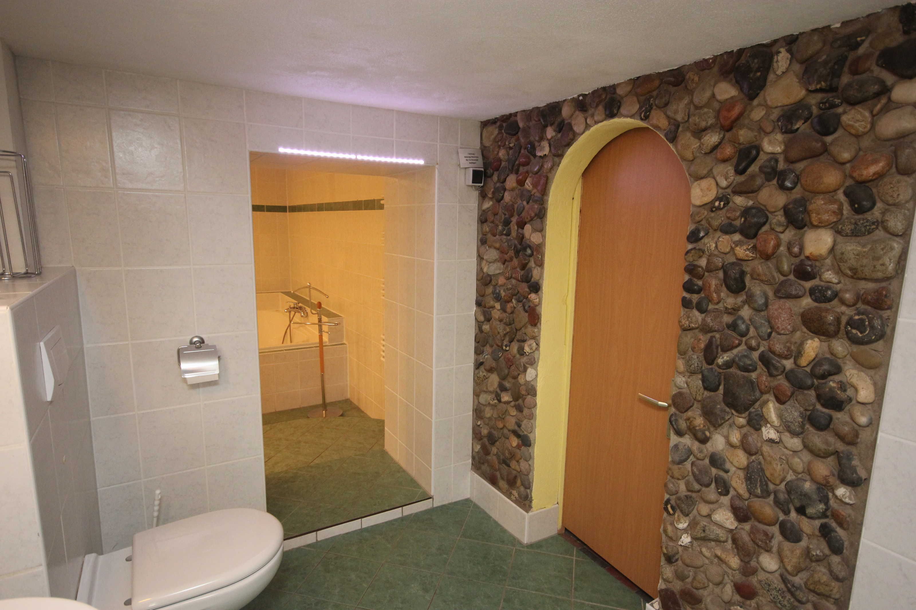 Une salle de bain avec des toilettes, une douche et un mur en pierre.