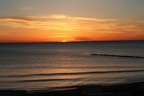 Un coucher de soleil sur une mer calme, avec une jetée qui s’avance dans l’eau.