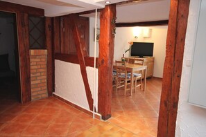Una habitación con estructura de vigas de madera, chimenea de ladrillo, una mesa de comedor con sillas y un televisor.