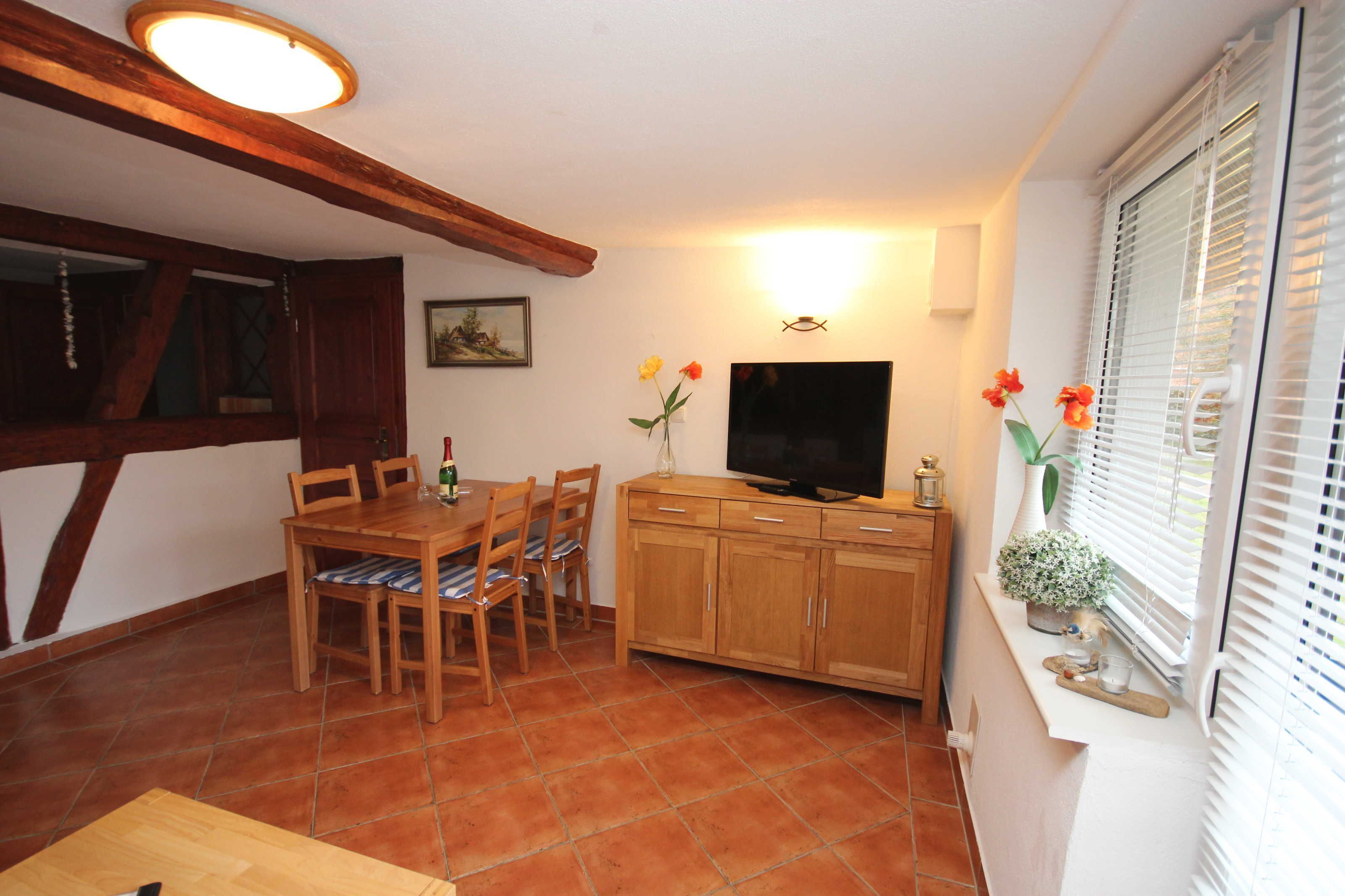 A dining area with a wooden table and chairs, a television, and a window with blinds.
