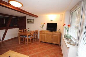 A dining area with a wooden table and chairs, a television, and a window with blinds.