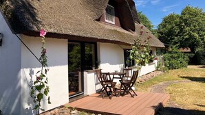 A thatched-roof house with a wooden deck and outdoor seating.