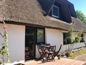 A house with a thatched roof, a sliding glass door, and a wooden deck with chairs.