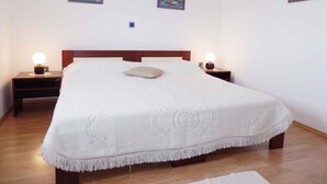A neatly made bed with a white blanket and a single pillow, flanked by two bedside tables with lamps, in a room with wooden flooring and white walls. - Holiday apartment with air conditioning and Internet (Medulin)