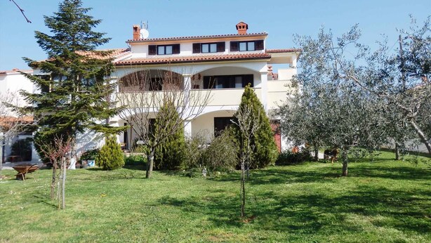 A two-story building with a tiled roof, surrounded by a well-maintained lawn and various trees. - Holiday apartment with air conditioning and Internet (Medulin)