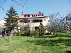 A two-story building with a tiled roof, surrounded by a well-maintained lawn and various trees. - Holiday apartment with air conditioning and Internet (Medulin)