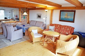 Un salon chaleureux avec des meubles en osier, une table à manger et une cuisine en arrière-plan.