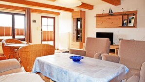 Una sala acogedora con una mesa de comedor, sillas de mimbre, un sofá y un televisor.