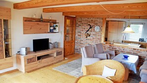 Una sala de estar acogedora con televisor, mueble de entretenimiento de madera, mobiliario de mimbre y una pared de ladrillo.