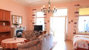Una sala de estar con sofá, televisor, chimenea y un ventanal con cortinas.