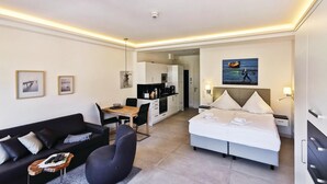 A modern hotel room with a bed, a sofa, a dining area, and a kitchen.