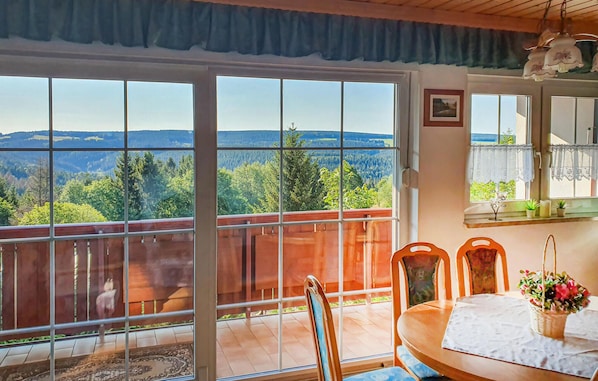 A balcony with a table and chairs, a view of a forested landscape, and a hanging light fixture.