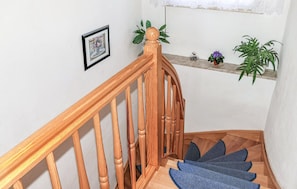 A wooden staircase with a handrail, a small shelf with plants, and a framed picture on the wall.