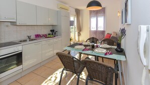 A modern kitchen with white cabinets, a built-in oven, and a dining area with wicker chairs and a glass table. - 2 bedroom beautiful apartment in Vodice (Vodice)