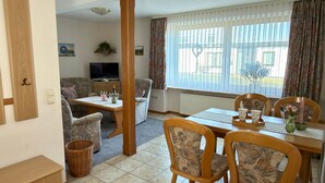 A furnished living room with a television, a dining table with chairs, a sofa, and a window with curtains. - Ferienhof Döring - Apartment Döring (Vöhl)