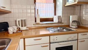 A kitchen with a microwave, coffee maker, kettle, toaster, and a window with a view of a building. - Ferienhof Döring - Apartment Döring (Vöhl)