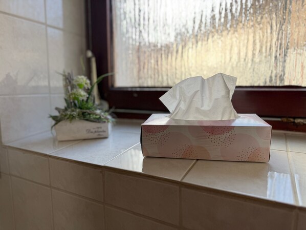 A tissue box on a tiled surface near a window with a frosted glass view.