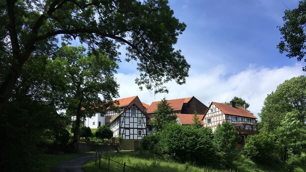 A traditional half-timbered house with a red roof, surrounded by lush greenery and a winding path. - Ferienhof Döring - Apartment Döring (Vöhl)