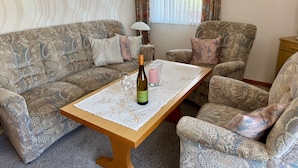 A living room with patterned sofas, a wooden coffee table, and a bottle of wine. - Ferienhof Döring - Apartment Döring (Vöhl)