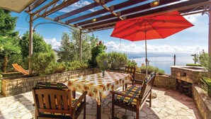 Une terrasse extérieure avec une table et des chaises, un parasol rouge et une vue sur la mer.
