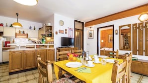 Un coin repas avec une nappe jaune, des chaises en bois et un téléviseur en arrière-plan.