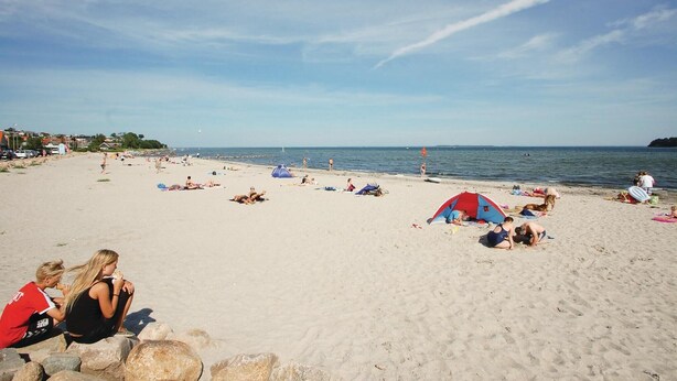 Ein Strand mit badenden Personen, Sonnenschirmen und Zelten.