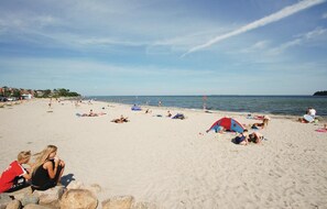 Een strand met mensen die zonnebaden en zwemmen, tenten en parasols.