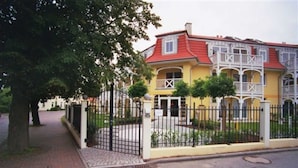 A yellow building with a red roof, white balconies, and a gated entrance.