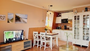 A living room with a TV, dining table, chairs, and a kitchen area with cabinets and a microwave.