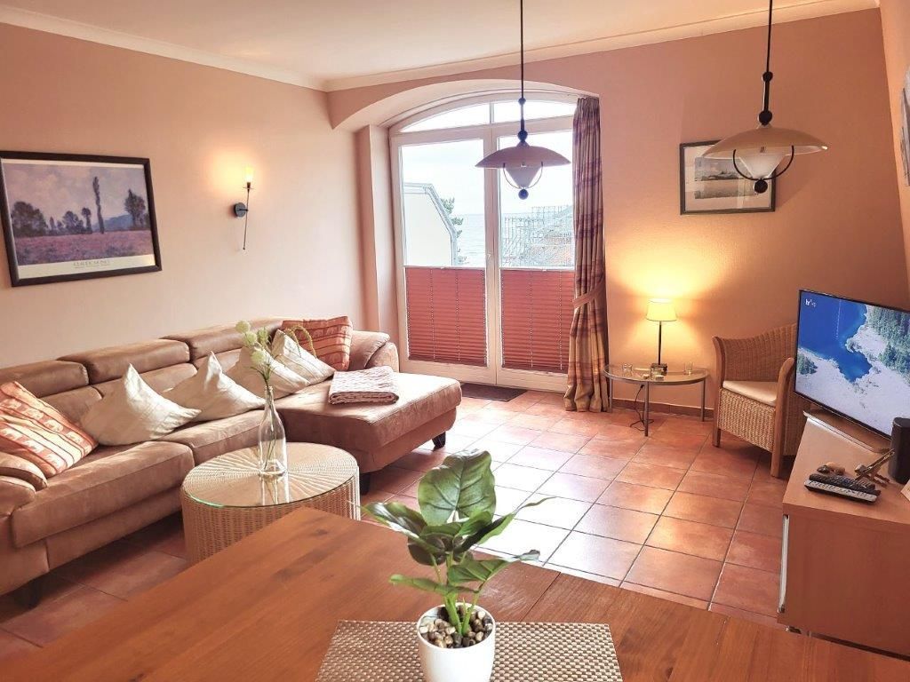 Ein gemütliches Wohnzimmer mit einer Couch, einem Couchtisch, einem Fernseher und einem großen Fenster mit Jalousien.