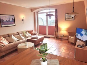 A cozy living room with a sofa, a coffee table, a TV, and a large window with blinds. - (190) 3-room apartment lake view - Apartment house Baltic Sea beach (Kühlungsborn)
