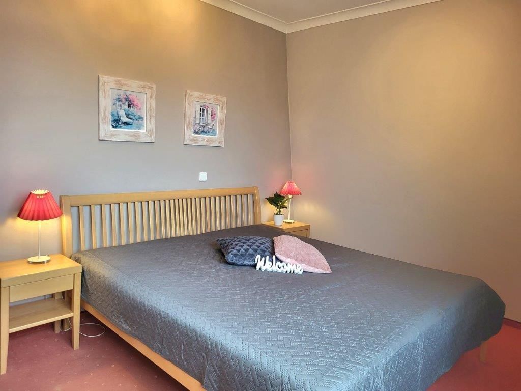 Een slaapkamer met een bed, twee wandlampen en twee ingelijste foto’s.