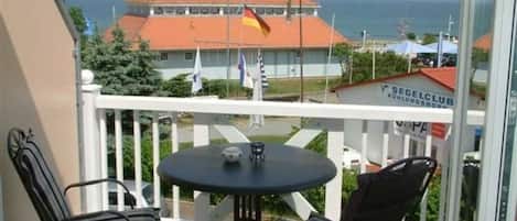 A balcony with two chairs and a table, overlooking a building with a red roof and flags.