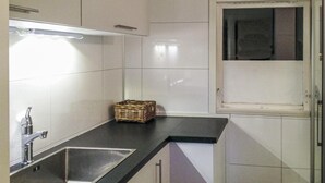 Una cocina con azulejos blancos, un fregadero de acero inoxidable, una cesta y una ventana con vistas.