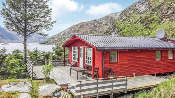 Una cabaña roja con un balcón, con vistas a un lago y montañas.